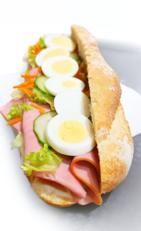 Belegd stokbrood met ham, gekookt ei, komkommer, geraspte wortel en sla op een bord