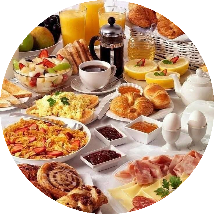 Ontbijttafel met fruitsalade, sinaasappelsap, koffie, croissants, roerei, jam, gekookte eieren, ham en kaas
